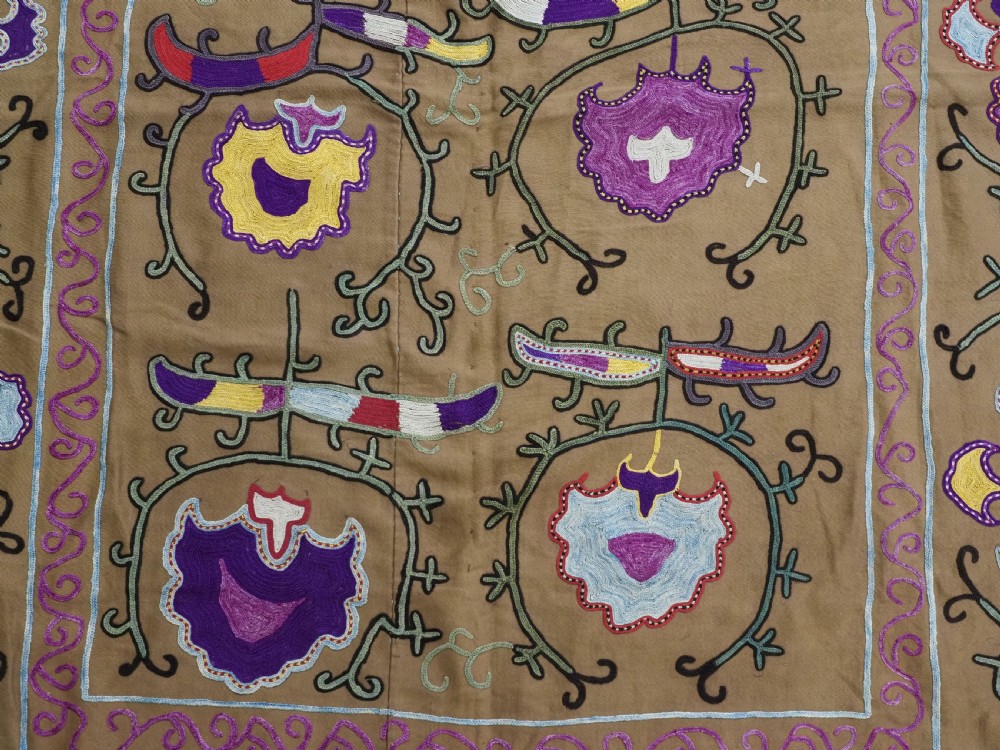 An antique Uzbek Nim Suzani textile featuring hand-embroidered floral motifs and hooked borders in purple, yellow, and blue silk threads on a tan cotton ground. View VII