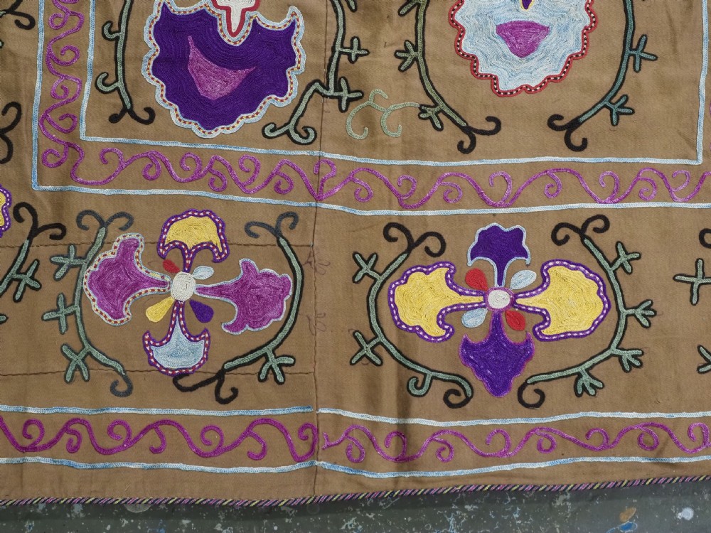 An antique Uzbek Nim Suzani textile featuring hand-embroidered floral motifs and hooked borders in purple, yellow, and blue silk threads on a tan cotton ground. View VIII