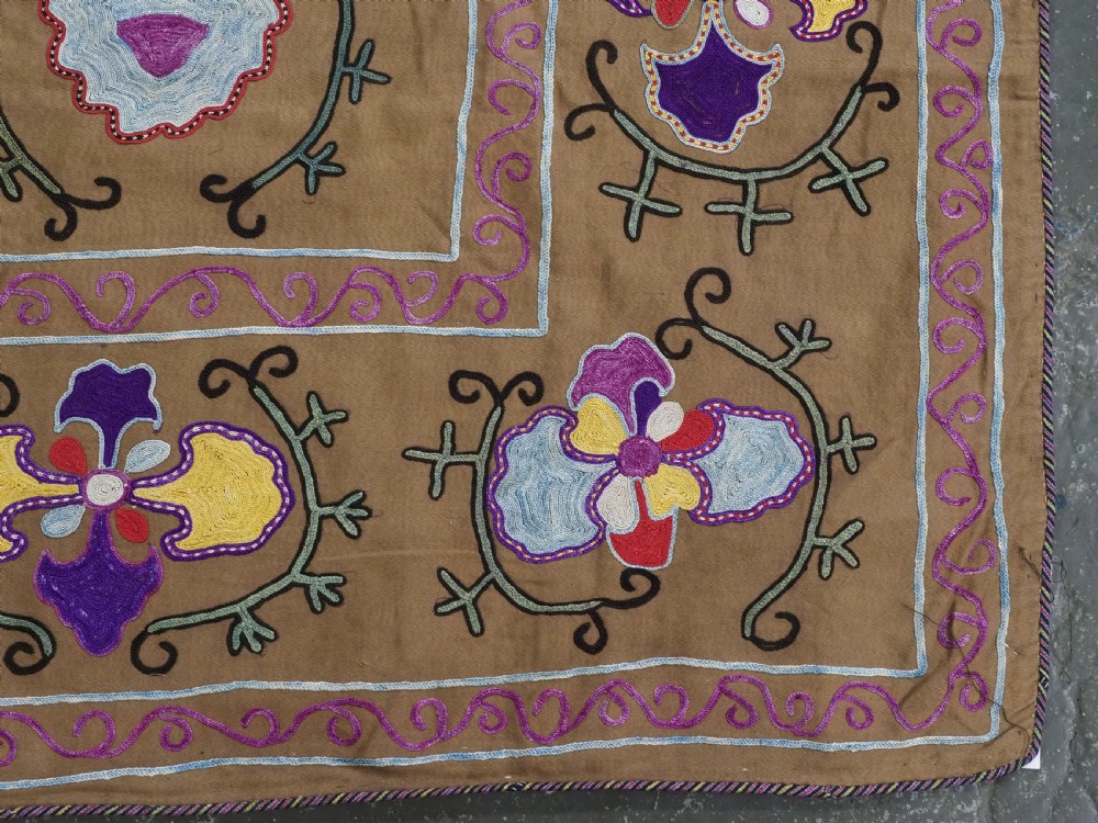 An antique Uzbek Nim Suzani textile featuring hand-embroidered floral motifs and hooked borders in purple, yellow, and blue silk threads on a tan cotton ground. View IX