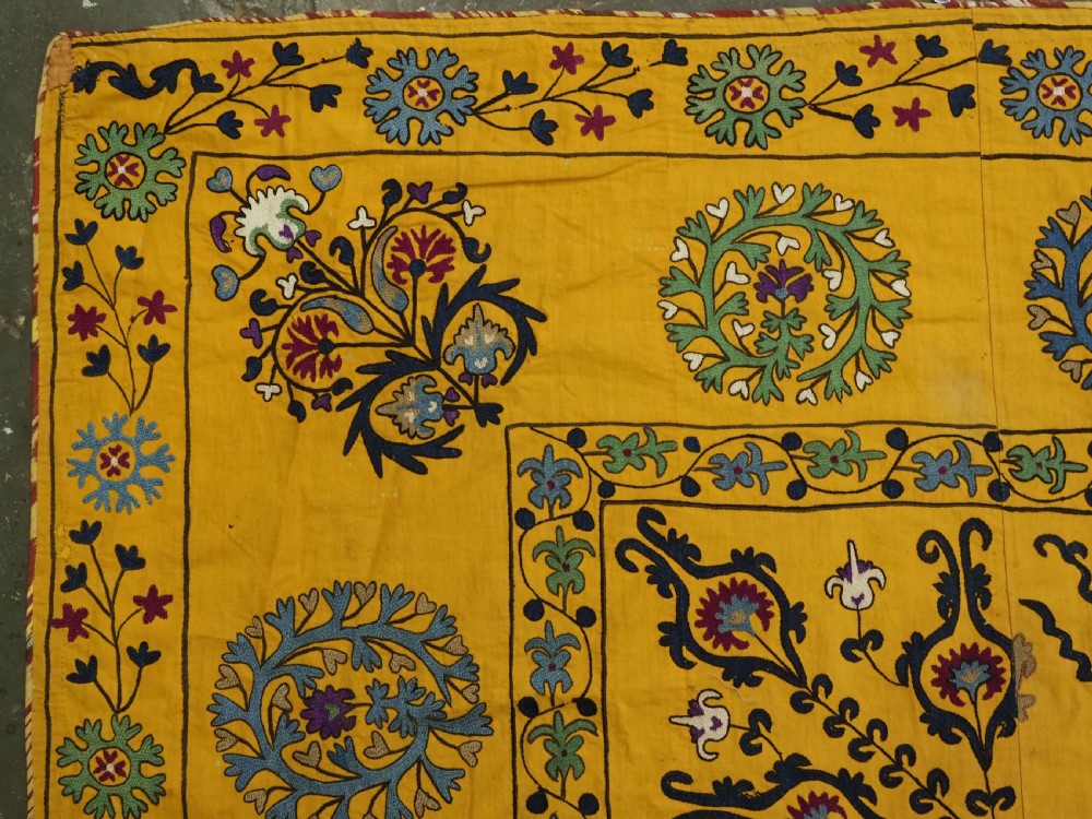 A rectangular yellow cotton textile featuring hand-embroidered silk floral medallions, vines, and circular motifs in blue, green, and burgundy. View II