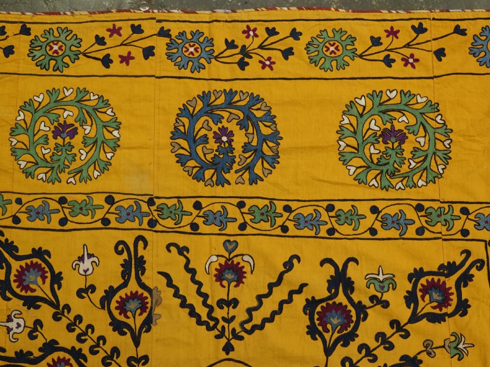 A rectangular yellow cotton textile featuring hand-embroidered silk floral medallions, vines, and circular motifs in blue, green, and burgundy. View IV