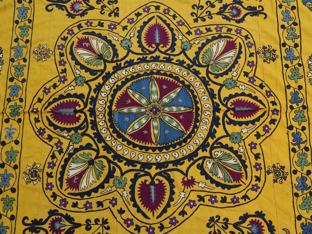 A rectangular yellow cotton textile featuring hand-embroidered silk floral medallions, vines, and circular motifs in blue, green, and burgundy. View V