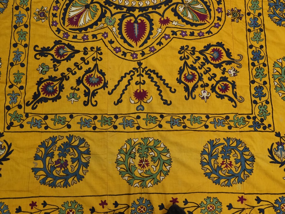 A rectangular yellow cotton textile featuring hand-embroidered silk floral medallions, vines, and circular motifs in blue, green, and burgundy. View VI