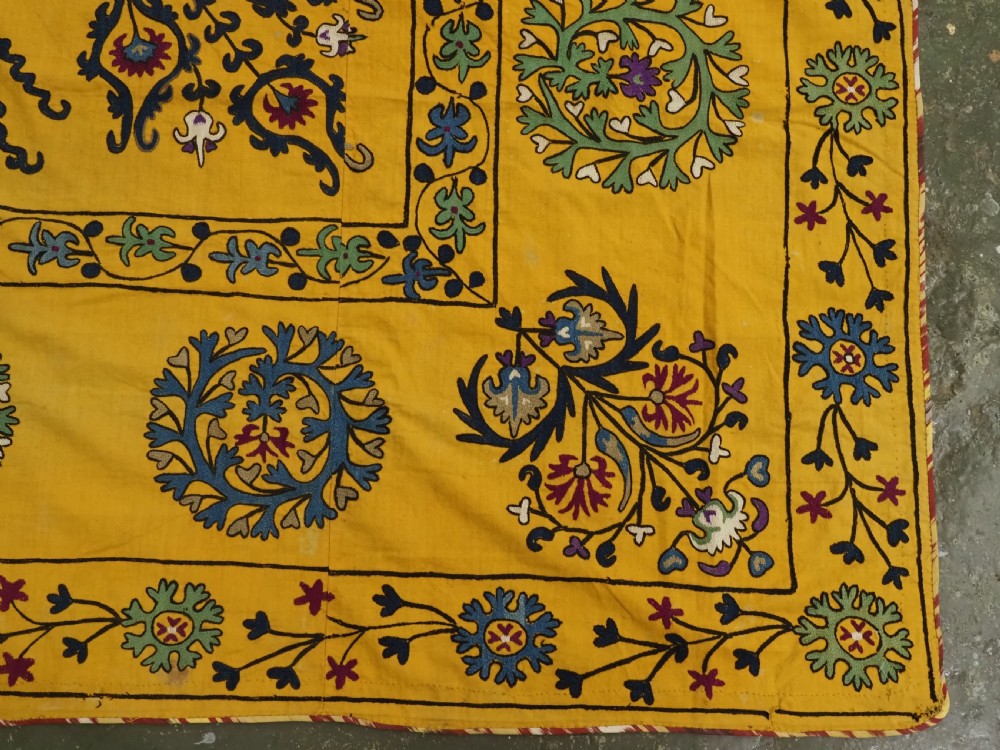 A rectangular yellow cotton textile featuring hand-embroidered silk floral medallions, vines, and circular motifs in blue, green, and burgundy. View VII