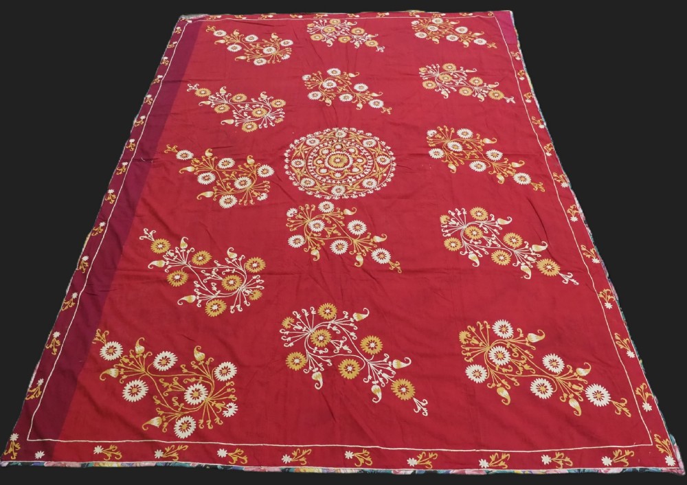 A rectangular red adras silk and cotton textile featuring yellow and white silk thread embroidery with a central circular floral medallion, surrounding floral sprays, and a matching decorative border.