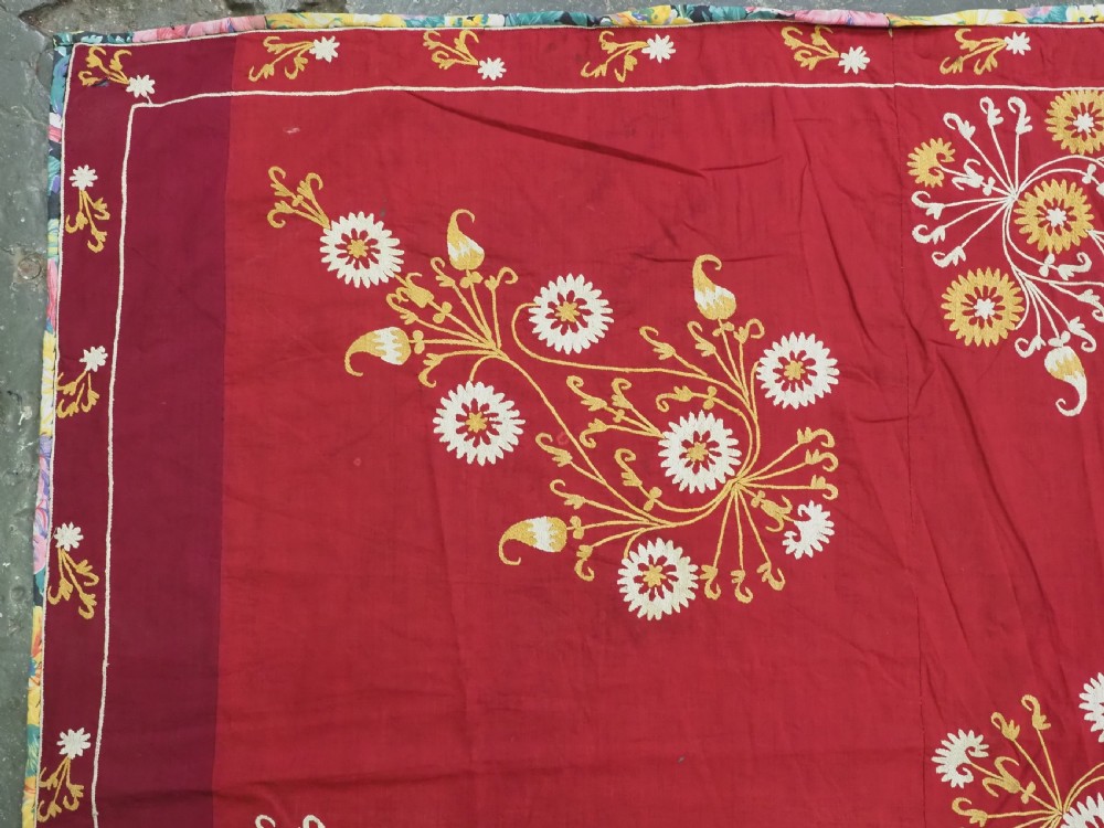 A rectangular red adras silk and cotton textile featuring yellow and white silk thread embroidery with a central circular floral medallion, surrounding floral sprays, and a matching decorative border. View V