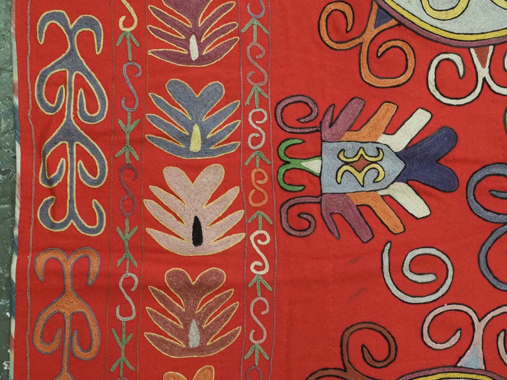 A rectangular red wool textile featuring multi-coloured silk embroidery with central circular medallions and decorative botanical borders. View V