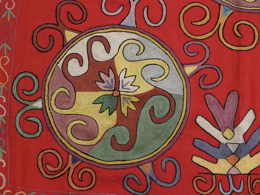 A rectangular red wool textile featuring multi-coloured silk embroidery with central circular medallions and decorative botanical borders. View VII