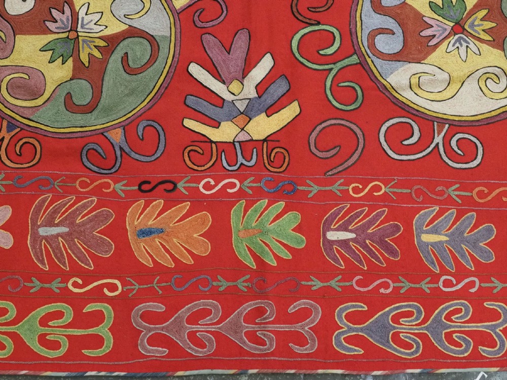A rectangular red wool textile featuring multi-coloured silk embroidery with central circular medallions and decorative botanical borders. View VIII