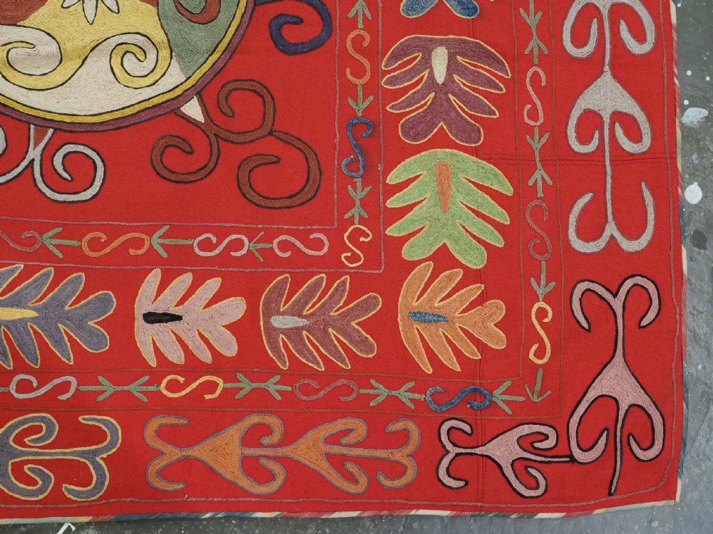 A rectangular red wool textile featuring multi-coloured silk embroidery with central circular medallions and decorative botanical borders. View IX