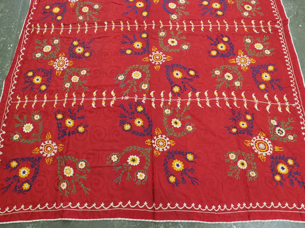 An antique rectangular red cotton suzani textile featuring hand embroidery in silk with floral rosettes and botanical motifs in white, yellow, green, and blue. View IV