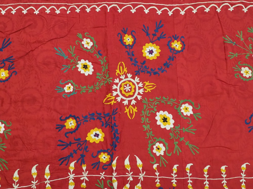 An antique rectangular red cotton suzani textile featuring hand embroidery in silk with floral rosettes and botanical motifs in white, yellow, green, and blue. View VI