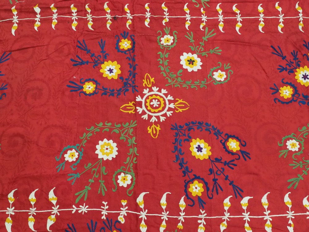 An antique rectangular red cotton suzani textile featuring hand embroidery in silk with floral rosettes and botanical motifs in white, yellow, green, and blue. View VIII