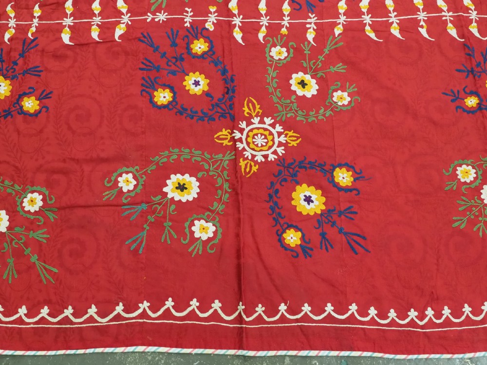 An antique rectangular red cotton suzani textile featuring hand embroidery in silk with floral rosettes and botanical motifs in white, yellow, green, and blue. View IX