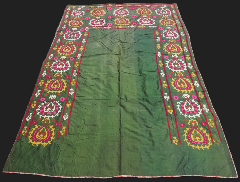 An antique green silk suzani bed cover featuring a plain central panel surrounded by a broad embroidered border with magenta, yellow, and white floral motifs.