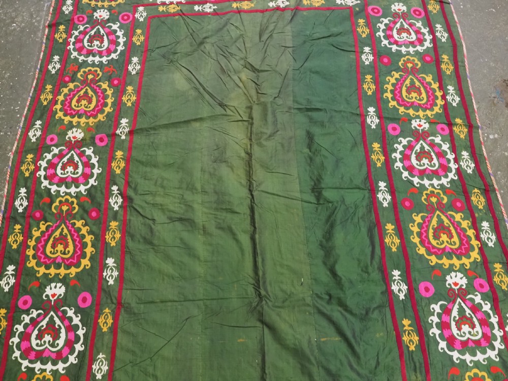 An antique green silk suzani bed cover featuring a plain central panel surrounded by a broad embroidered border with magenta, yellow, and white floral motifs. View III