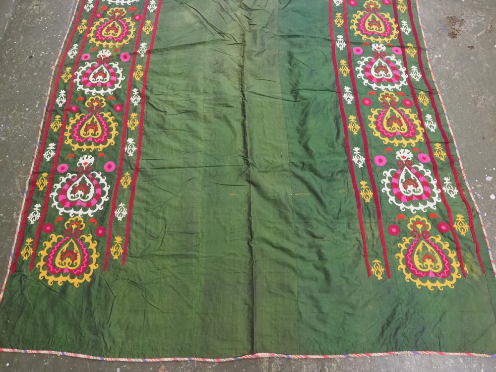 An antique green silk suzani bed cover featuring a plain central panel surrounded by a broad embroidered border with magenta, yellow, and white floral motifs. View IV