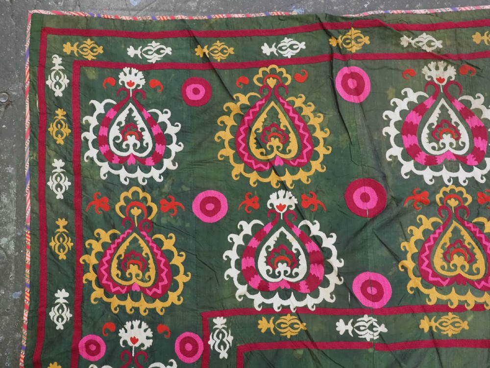 An antique green silk suzani bed cover featuring a plain central panel surrounded by a broad embroidered border with magenta, yellow, and white floral motifs. View V