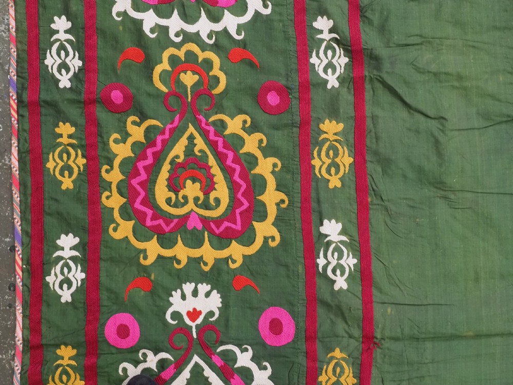 An antique green silk suzani bed cover featuring a plain central panel surrounded by a broad embroidered border with magenta, yellow, and white floral motifs. View VI
