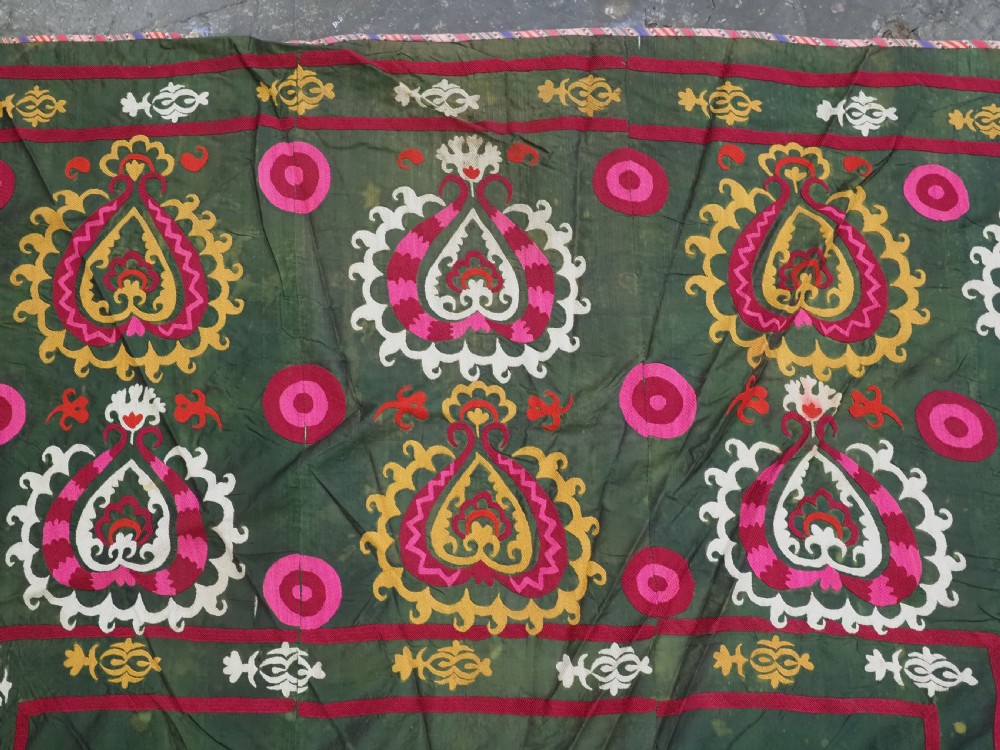 An antique green silk suzani bed cover featuring a plain central panel surrounded by a broad embroidered border with magenta, yellow, and white floral motifs. View VII