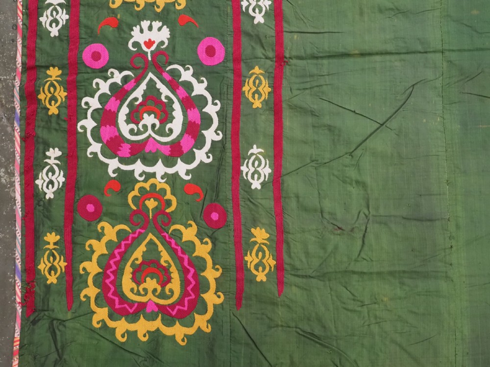 An antique green silk suzani bed cover featuring a plain central panel surrounded by a broad embroidered border with magenta, yellow, and white floral motifs. View VIII
