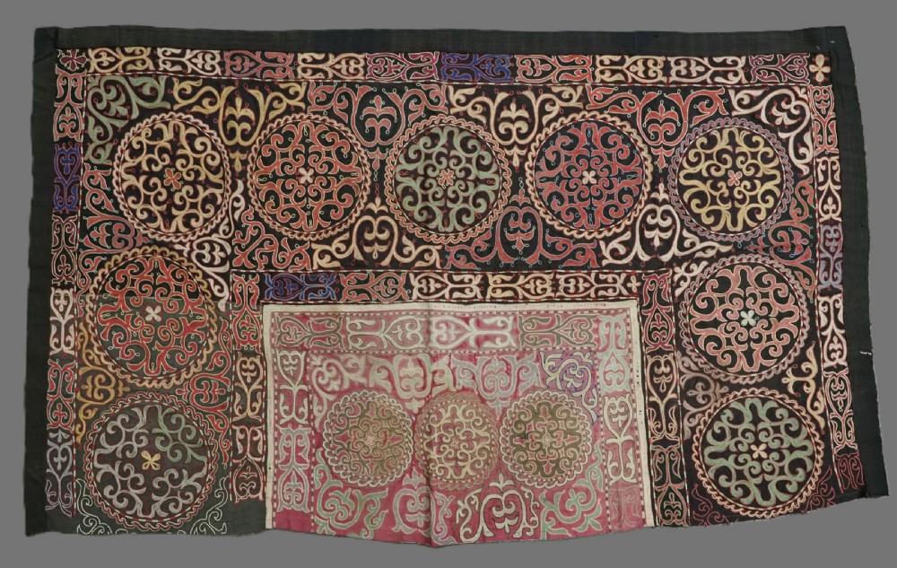 An antique Kyrgyz tush kyiz embroidered wall hanging featuring circular scrollwork medallions and geometric borders in red, pink, and white thread against a dark background.
