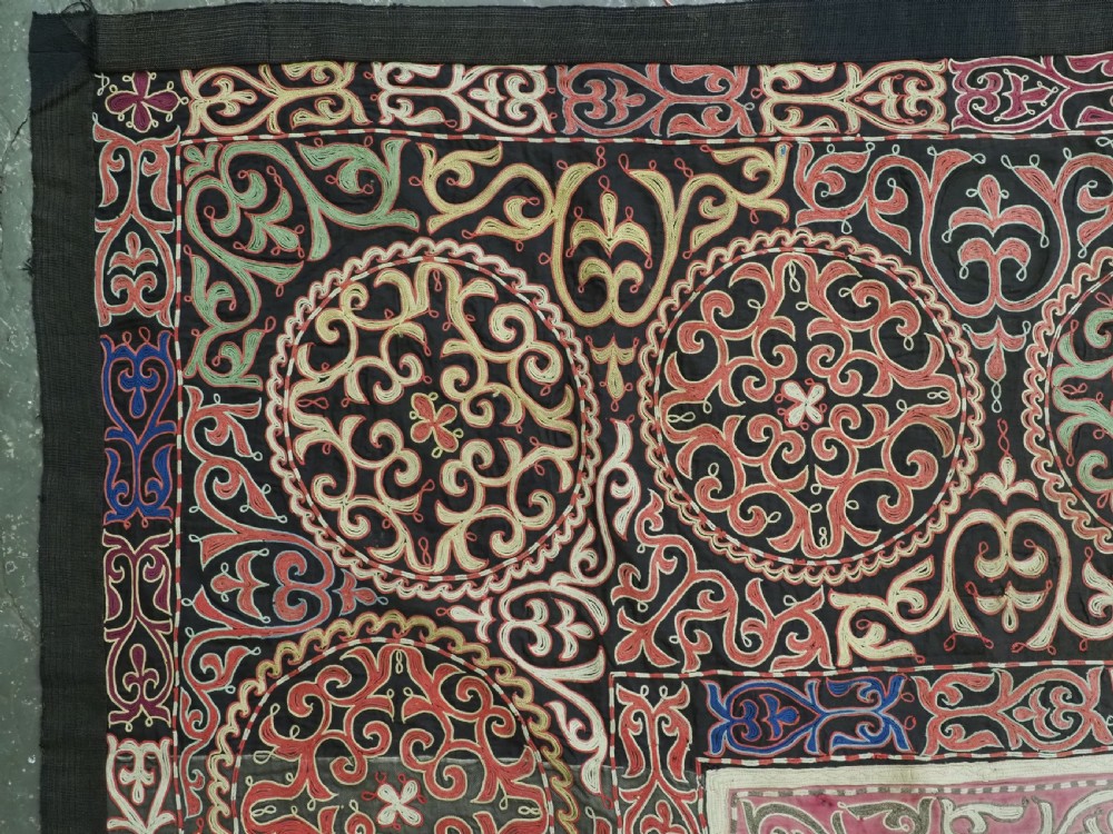 An antique Kyrgyz tush kyiz embroidered wall hanging featuring circular scrollwork medallions and geometric borders in red, pink, and white thread against a dark background. View II