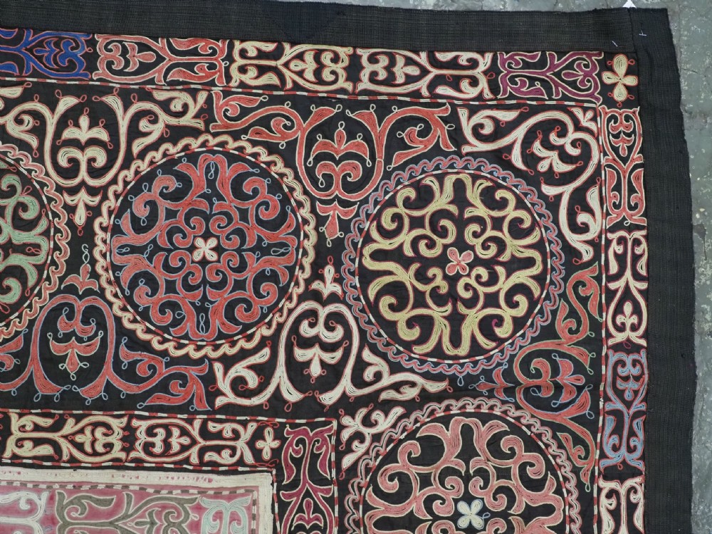An antique Kyrgyz tush kyiz embroidered wall hanging featuring circular scrollwork medallions and geometric borders in red, pink, and white thread against a dark background. View IV