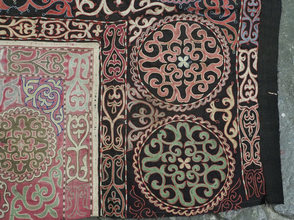 An antique Kyrgyz tush kyiz embroidered wall hanging featuring circular scrollwork medallions and geometric borders in red, pink, and white thread against a dark background. View VII