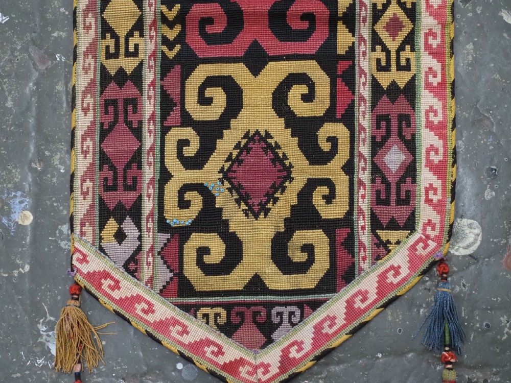 An antique Uzbek Lakai hand-embroidered wool textile featuring geometric horn motifs, a pointed lower hem, and multi-coloured yarn tassels. View V