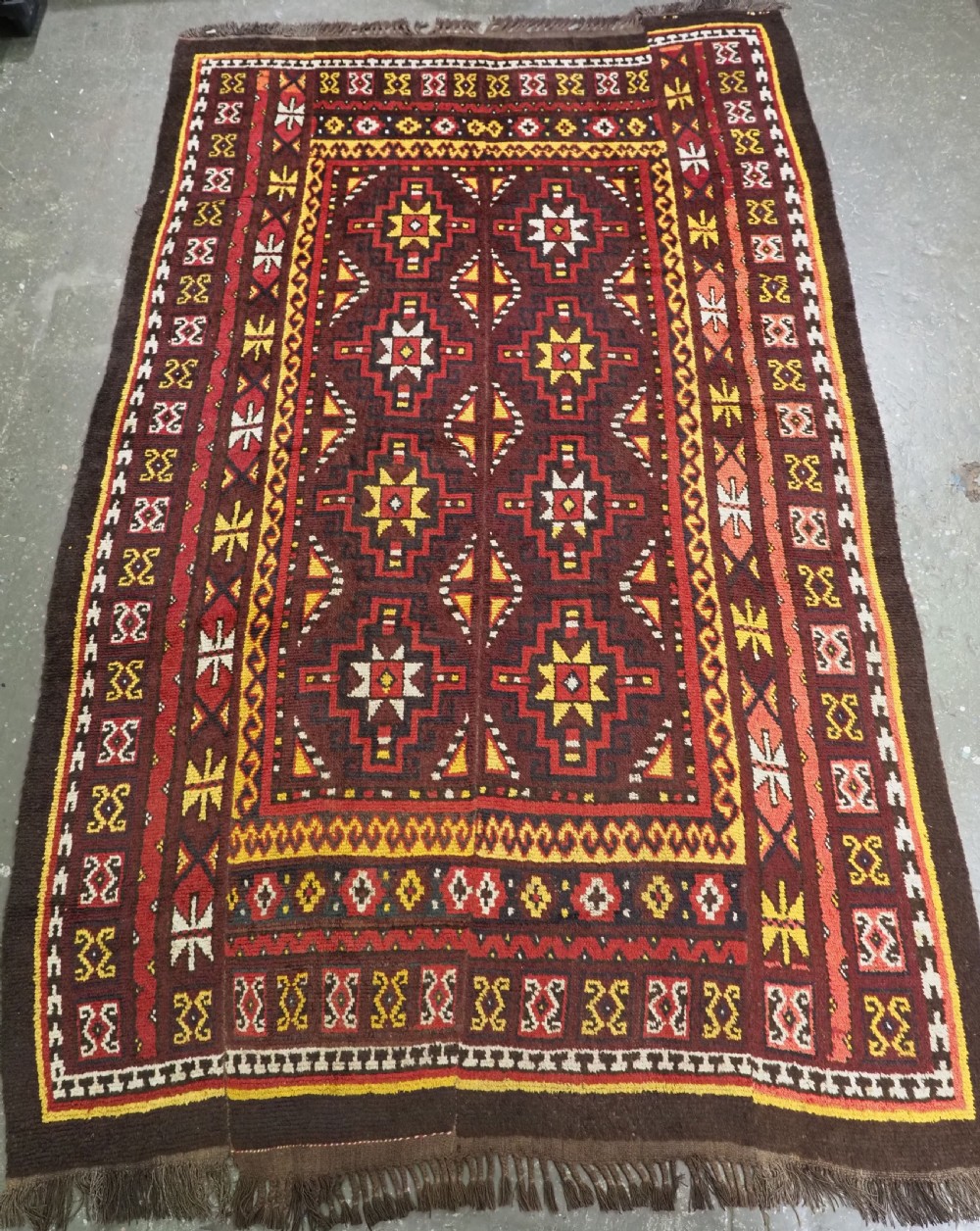 An antique handwoven Uzbek Julkyrs rug with geometric star motifs constructed from four vertical wool strips stitched together in tones of brown, red, and yellow.