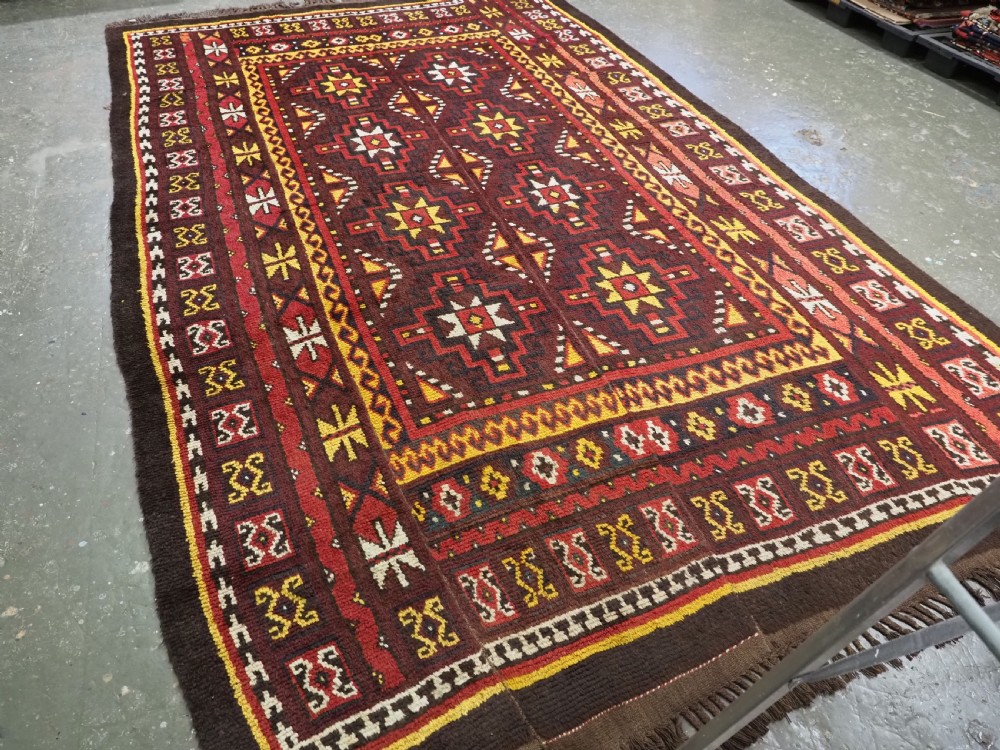 An antique handwoven Uzbek Julkyrs rug with geometric star motifs constructed from four vertical wool strips stitched together in tones of brown, red, and yellow. View II
