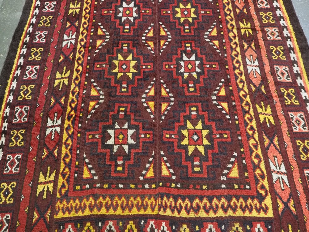 An antique handwoven Uzbek Julkyrs rug with geometric star motifs constructed from four vertical wool strips stitched together in tones of brown, red, and yellow. View V