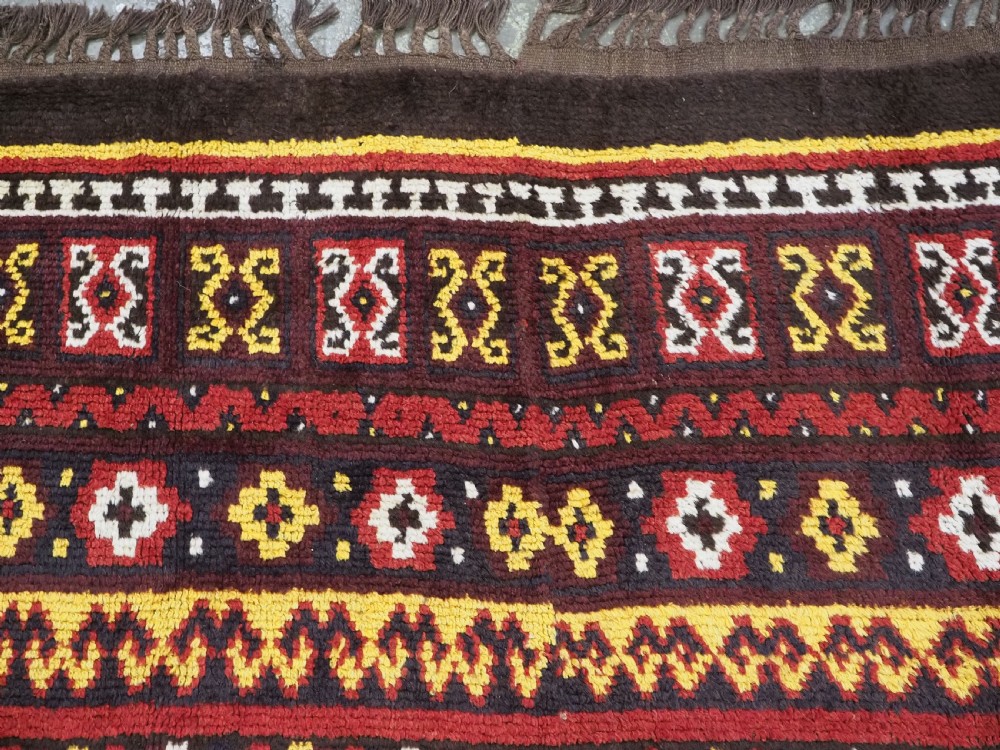 An antique handwoven Uzbek Julkyrs rug with geometric star motifs constructed from four vertical wool strips stitched together in tones of brown, red, and yellow. View X