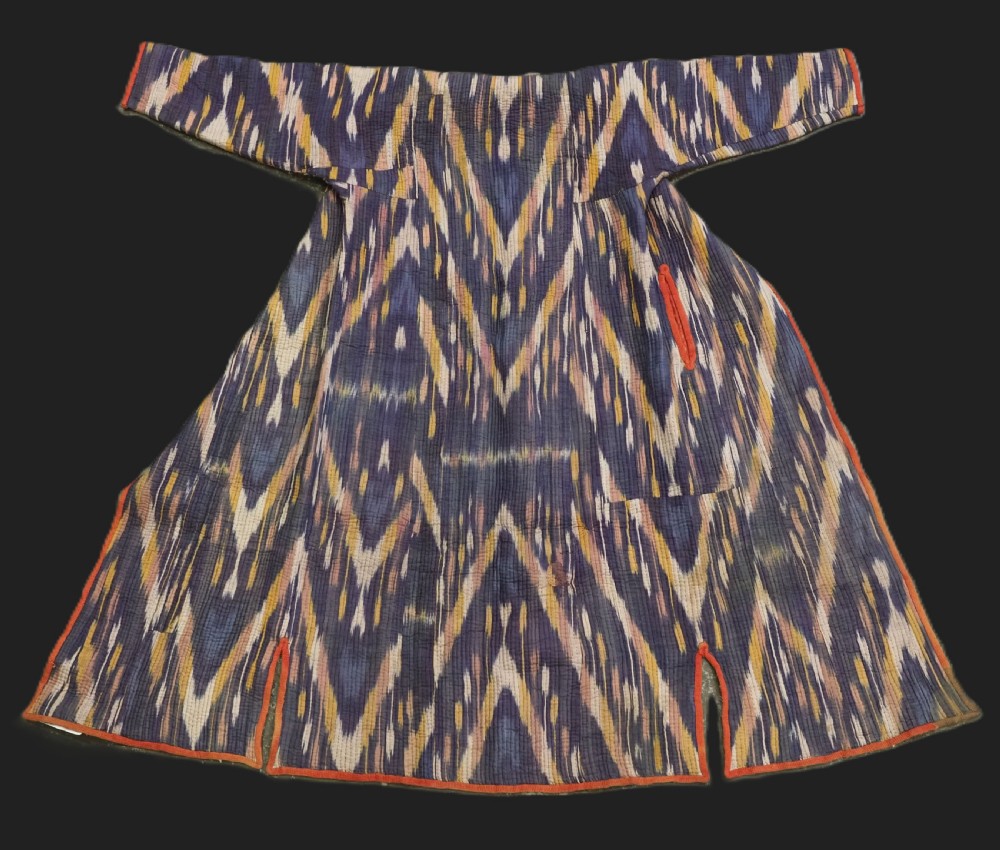 A quilted late 19th-century Uzbek silk ikat chapan coat featuring a bold chevron motif in indigo blue, yellow, and white, framed with red edge trimming.