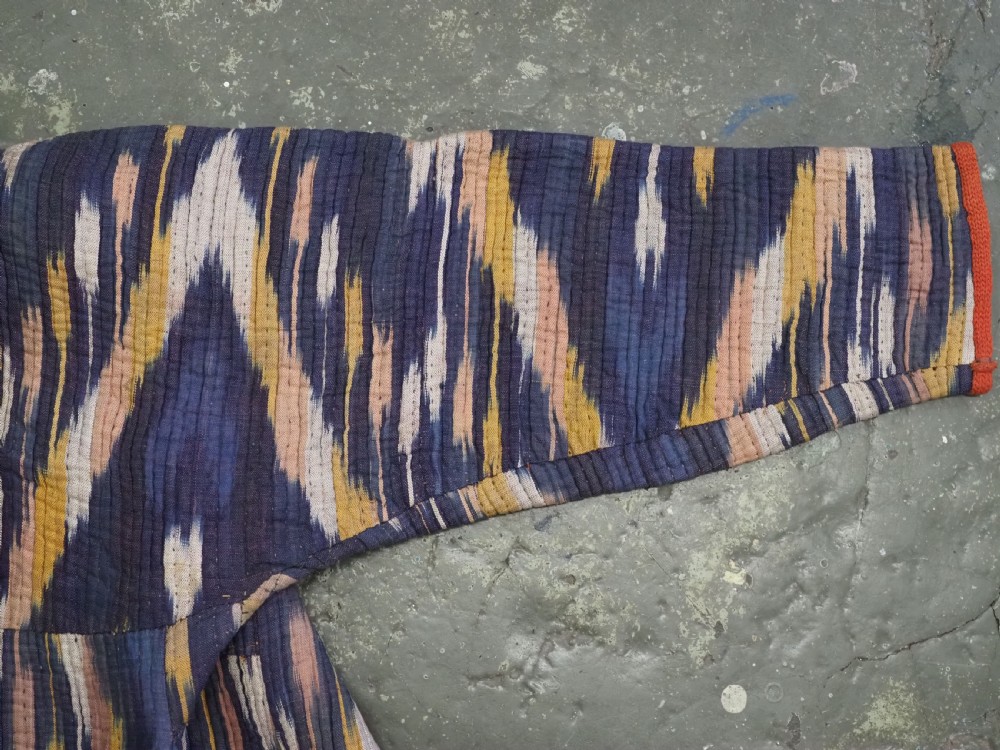 A quilted late 19th-century Uzbek silk ikat chapan coat featuring a bold chevron motif in indigo blue, yellow, and white, framed with red edge trimming. View VI