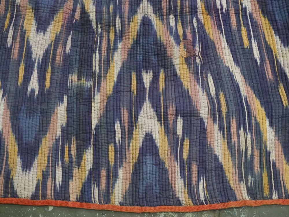A quilted late 19th-century Uzbek silk ikat chapan coat featuring a bold chevron motif in indigo blue, yellow, and white, framed with red edge trimming. View VII