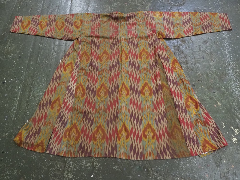 An antique Uzbek silk ikat coat featuring repeating diamond pattern motifs in red, yellow, green, and purple shades with flared sleeves. View II