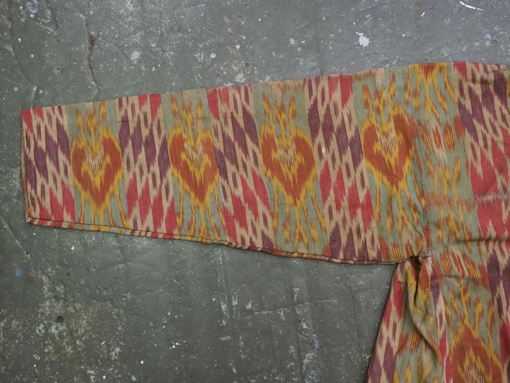 An antique Uzbek silk ikat coat featuring repeating diamond pattern motifs in red, yellow, green, and purple shades with flared sleeves. View III