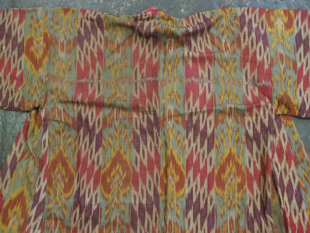 An antique Uzbek silk ikat coat featuring repeating diamond pattern motifs in red, yellow, green, and purple shades with flared sleeves. View V