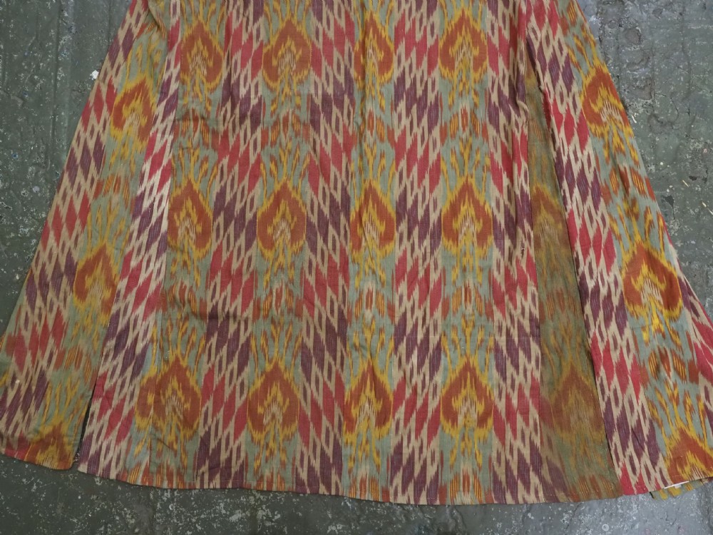 An antique Uzbek silk ikat coat featuring repeating diamond pattern motifs in red, yellow, green, and purple shades with flared sleeves. View VI