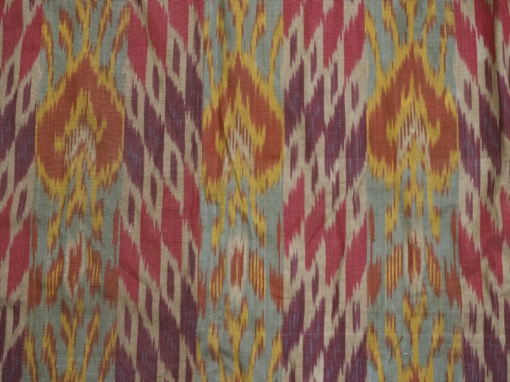 An antique Uzbek silk ikat coat featuring repeating diamond pattern motifs in red, yellow, green, and purple shades with flared sleeves. View VII