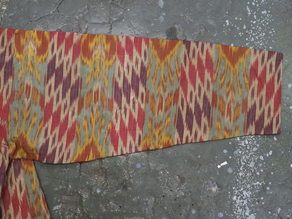 An antique Uzbek silk ikat coat featuring repeating diamond pattern motifs in red, yellow, green, and purple shades with flared sleeves. View VIII