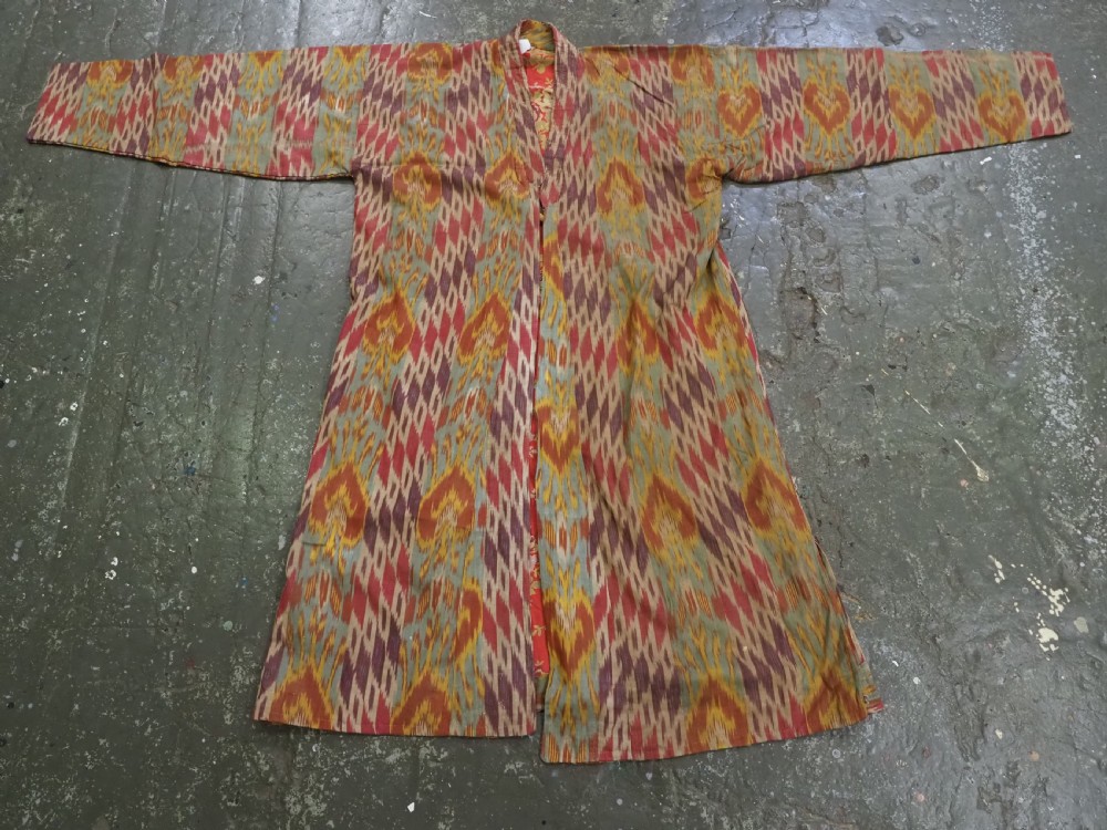 An antique Uzbek silk ikat coat featuring repeating diamond pattern motifs in red, yellow, green, and purple shades with flared sleeves. View IX