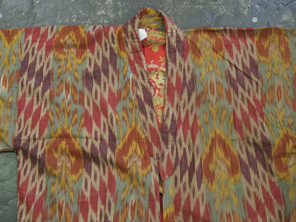 An antique Uzbek silk ikat coat featuring repeating diamond pattern motifs in red, yellow, green, and purple shades with flared sleeves. View X