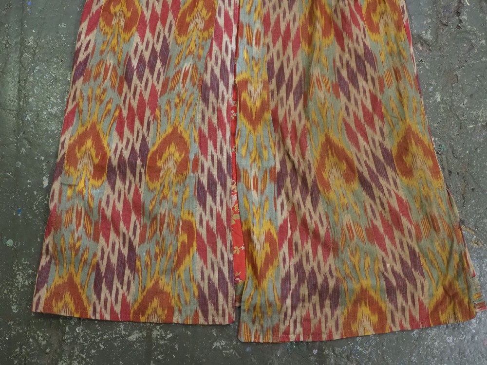 An antique Uzbek silk ikat coat featuring repeating diamond pattern motifs in red, yellow, green, and purple shades with flared sleeves. View XI