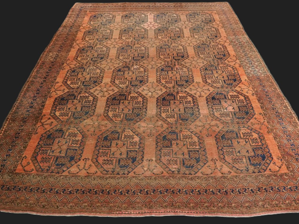 An antique hand-knotted wool carpet featuring repeating octagonal gul motifs on a terracotta background framed by geometric borders.