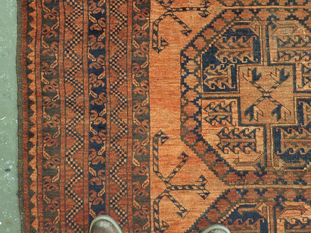 An antique hand-knotted wool carpet featuring repeating octagonal gul motifs on a terracotta background framed by geometric borders. View VII