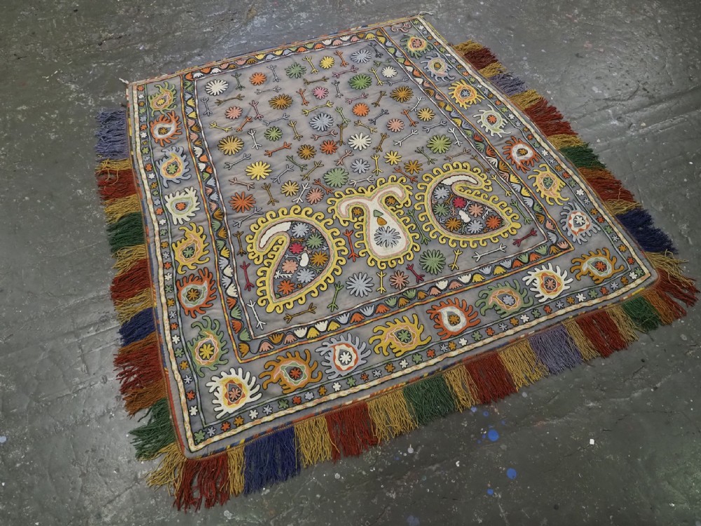 An early 20th-century Uzbek Lakai embroidered saddle cover featuring vibrant silk boteh and floral motifs on a grey ground with colourful fringe trim. View II