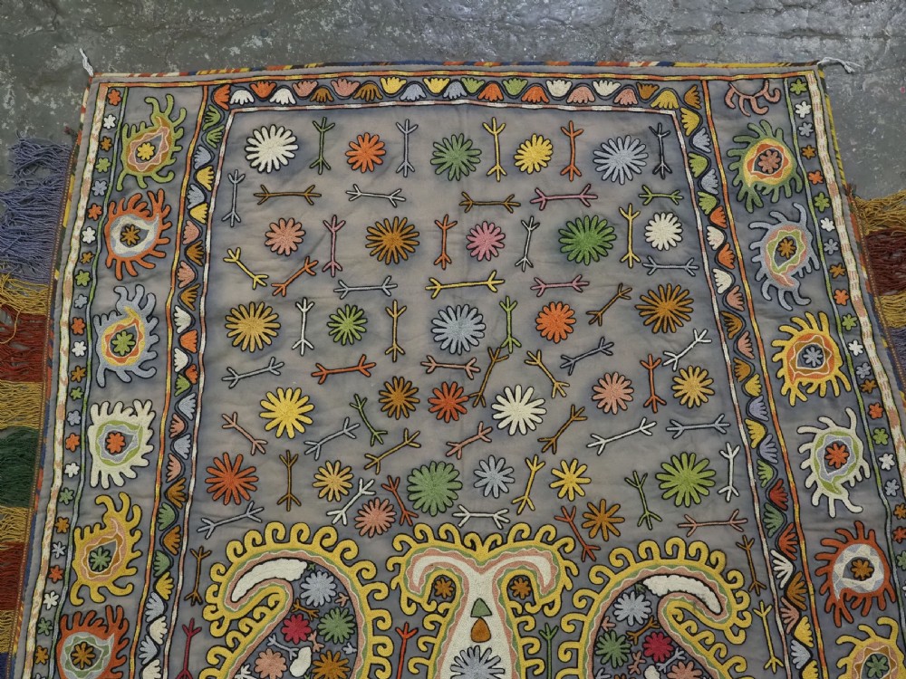An early 20th-century Uzbek Lakai embroidered saddle cover featuring vibrant silk boteh and floral motifs on a grey ground with colourful fringe trim. View III